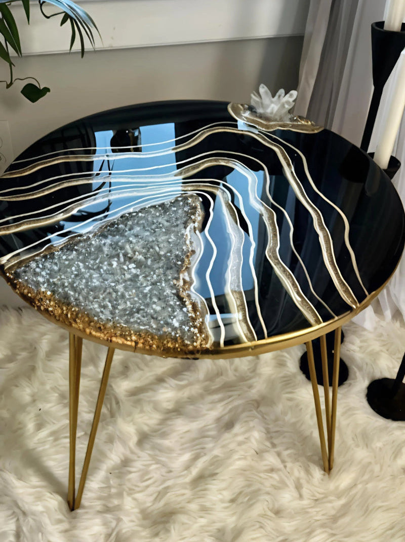 Round side table with black and gold design in a room with plants and a window.