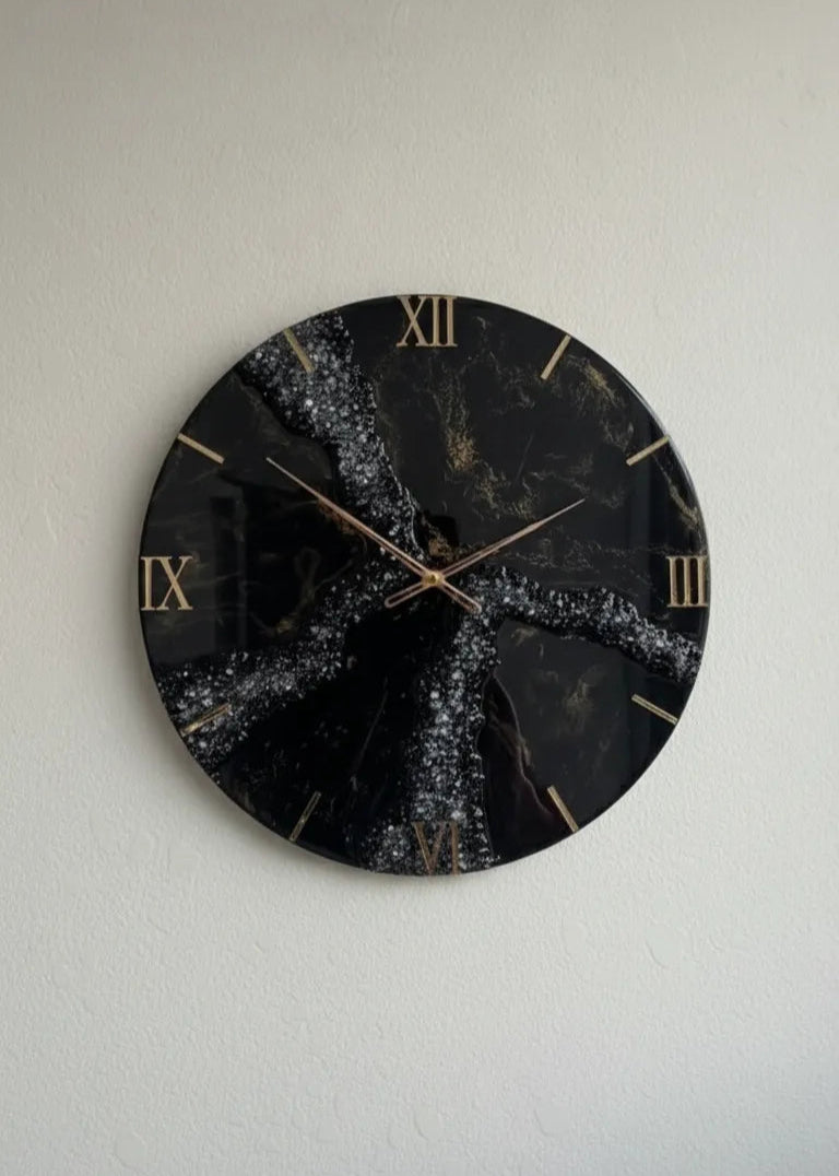 Decorative wall clock with black face and gold accents on a light gray wall.